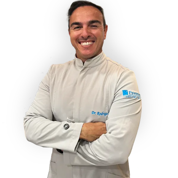 Dr. Rodrigo Garbim sorrindo, de braços cruzados, com o jaleco claro da Premier