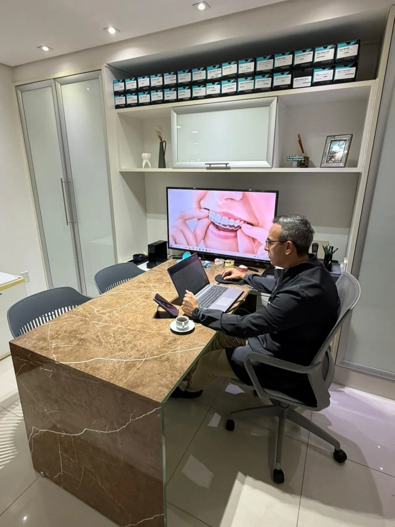 Dr. Rodrigo Garbim trabalhando no computador, na mesa de mármore de um consultório da clínica nova