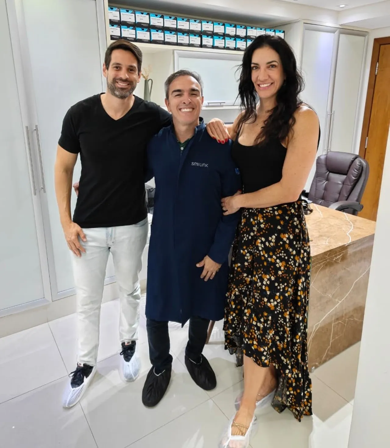 Dr. Rodrigo Garbim, de uniforme azul-marinho, com duas visitas no consultório da clínica nova